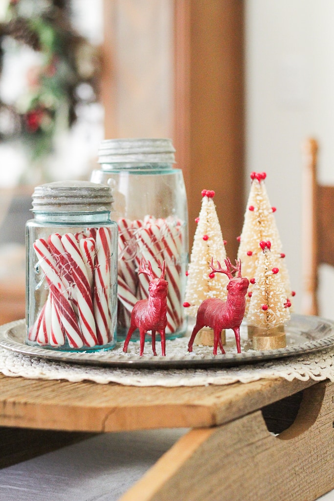 Wood sleigh centerpiece with a tray filled with blue ball jars with candy canes, antique red deer and red and white bottle brush trees.